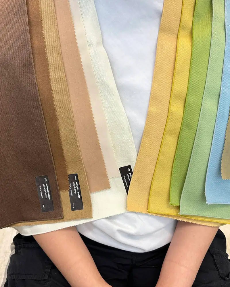 A woman displays a variety of colorful fabrics, showcasing different textures and patterns in her hands.