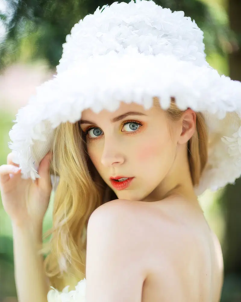 A young woman with a radiant smile wearing a stylish white hat, set against a soft, blurred background.