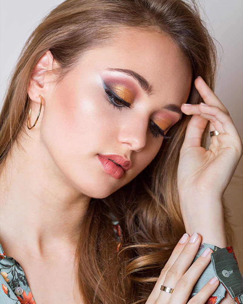 A woman showcasing vibrant gold and orange eye shadow, enhancing her eyes with a bold and colorful makeup look.